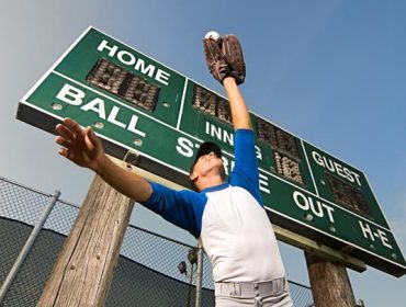 A portrait photo of a baseball player catches the ball under the scoreboard