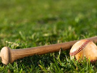 A landscape photo of a baseball bat's grip end with a baseball in front of it lying on grass